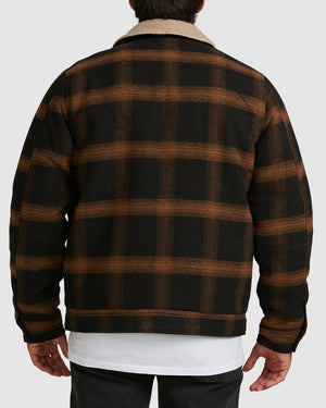 A person seen from behind wears the Billabong Barlow Sherpa Jacket, featuring black and brown plaid with a white sherpa collar. Their arms are relaxed by their sides, paired with a white shirt and black pants.