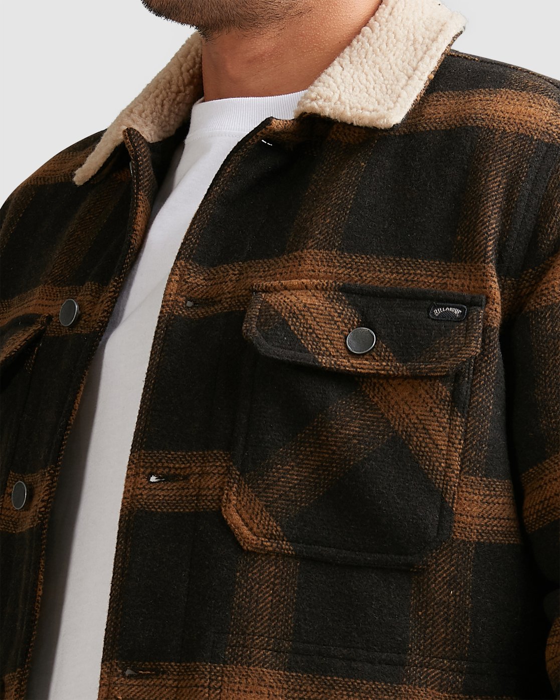 A person wears the Billabong Barlow Sherpa Jacket, featuring a black and brown plaid design, cream sherpa collar, and front flap pockets with metal snaps, over a white shirt. The image shows only the upper torso.