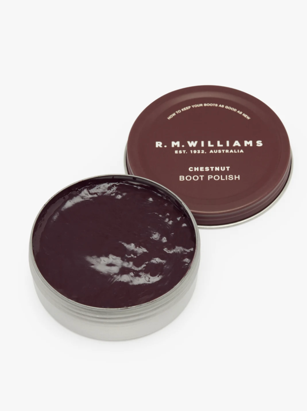 A round tin of RM Williams Stockmans Boot Polish with a brown lid placed beside it. The dark brown, glossy boot polish inside the tin features an alcohol-free formula to restore color and shine. The lid is branded with the RM Williams logo and some text.