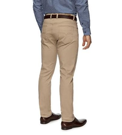 A person wearing a pair of City Club Austin Road Pants in slim fit beige khaki, paired with a dark brown belt featuring a woven pattern, a blue dress shirt adorned with a small white dot pattern, and brown dress shoes is shown from the back, standing upright.