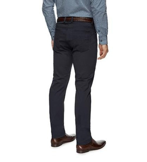 A person wearing stylish City Club Austin Road Pant in dark blue, complemented by brown shoes, a brown belt, and a light blue patterned long-sleeve shirt. The image is taken of the person's lower back and legs from behind. The ensemble looks perfect for a day out at the City Club.
