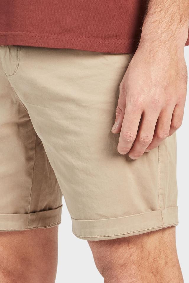A close-up image of a man's hand and lower torso wearing the Academy Brand Cooper Chino Short in tan and a comfortable reddish-brown shirt. The details of the shorts and part of the shirt are visible against a plain white background.