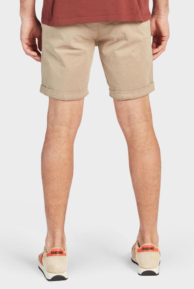 Back view of a person wearing a red-brown T-shirt, light beige Academy Brand Cooper Chino Short rolled up, and white sneakers with orange accents. The person's hands are placed by their sides, and they are standing against a plain white background.