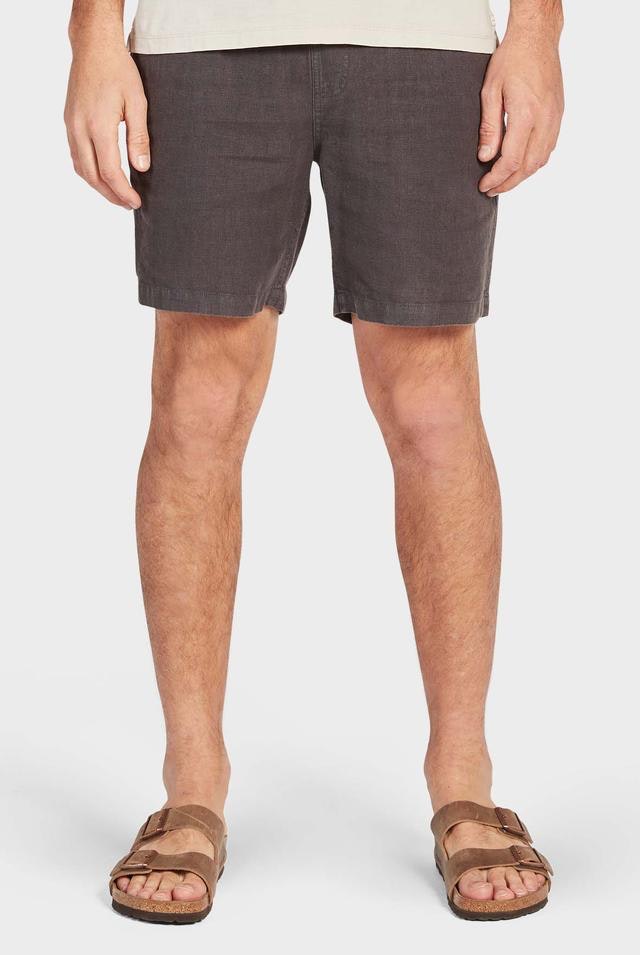 The image depicts the lower half of a person dressed in Academy Brand Riviera Linen Shorts and brown sandals with dual straps, set against a light background. The relaxed-fit shorts feature a simple, casual design with an elastic waist.