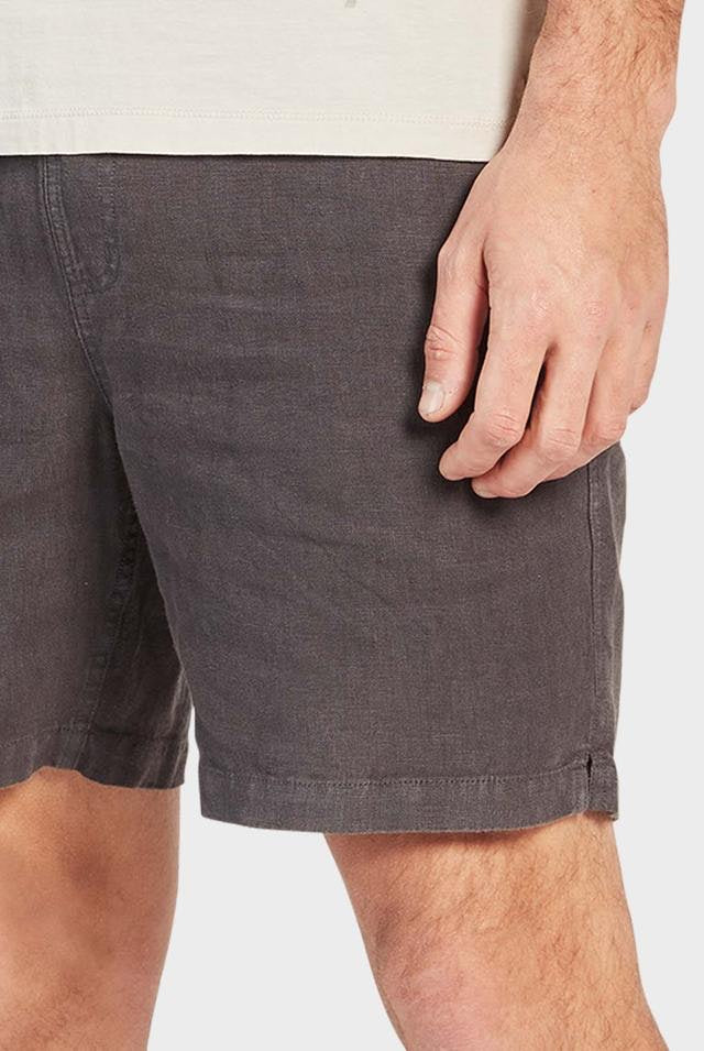 Wearing a light-colored shirt, someone pairs it effortlessly with Academy Brand Riviera Linen Short in dark gray. The image zooms in on the shorts' relaxed fit and textured fabric, featuring an elastic waist against a plain white backdrop.