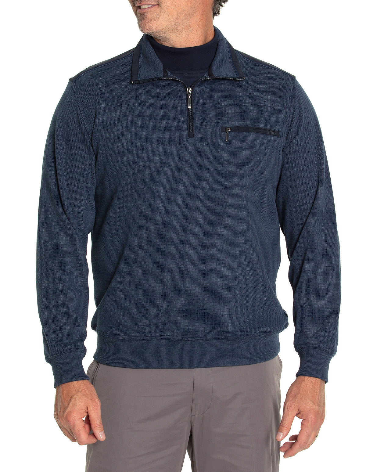 A person wearing a Breakaway Ryan Half Zip Fleece in dark blue, featuring a comfortable fit with a half-zip front and a zippered chest pocket, stands with hands relaxed at their sides. The person is also wearing gray pants and a black undershirt. The background is plain and white.