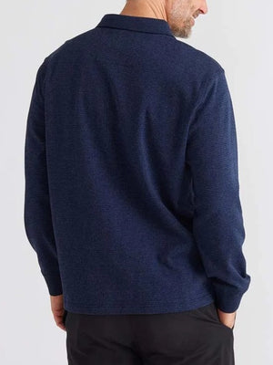 Rear view of a person wearing the relaxed fit Breakaway Micro Check Micro Prima Polo, a navy blue long-sleeve shirt paired with black pants against a light gray background. The individual has short hair and a beard.