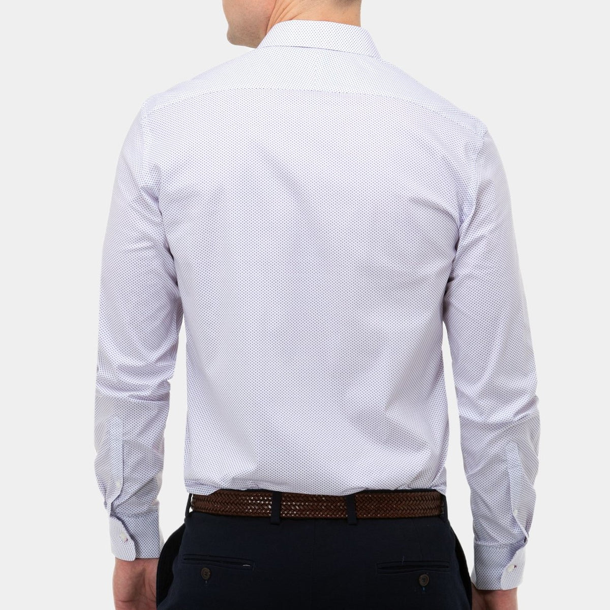A man is shown from behind, wearing a stylish Brooksfield Stretch Print Shirt with a subtle dotted pattern. The shirt is neatly tucked into dark navy pants, secured with a brown woven leather belt. The background is plain and unobtrusive, emphasizing the clothing.