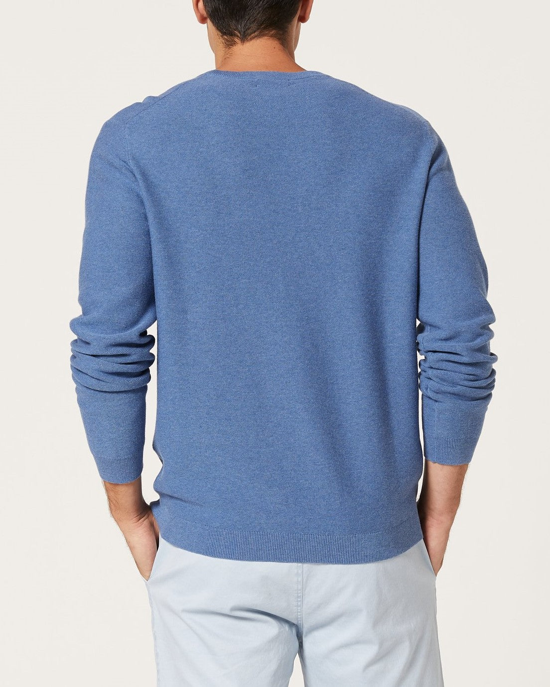 A man is seen from behind wearing the Blazer Mason Cotton Crew Neck in blue and light pants, standing with hands in pockets against a plain light background.