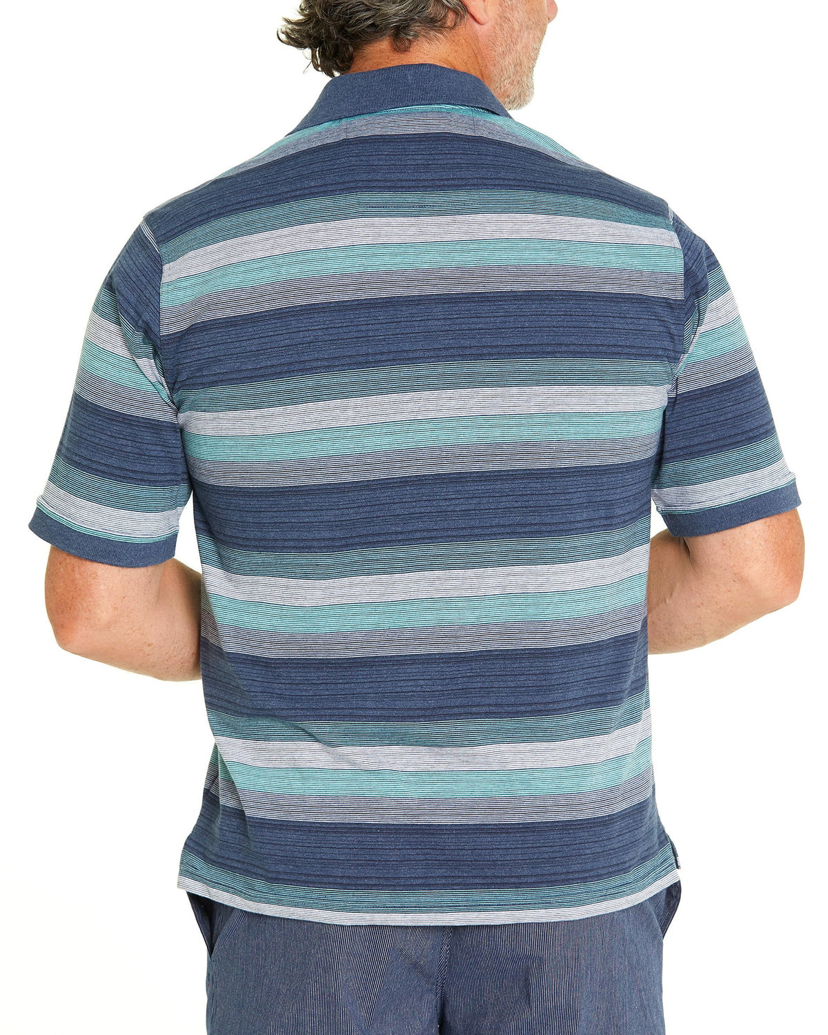 A man in a Breakaway Otto Kinnersly Jersey Polo with horizontal green, blue, and gray stripes stands with his back facing the camera. He is wearing blue pants against a plain white background. The classic collar of the polo adds a touch of refinement to his relaxed look.