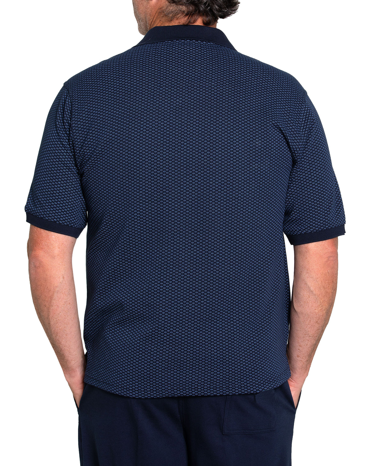 Rear view of a person wearing a Breakaway Diamond Micro Prima Polo, featuring a dark blue pattern and classic collar, paired with dark trousers. Their hands are tucked into their pockets against a crisp white background.