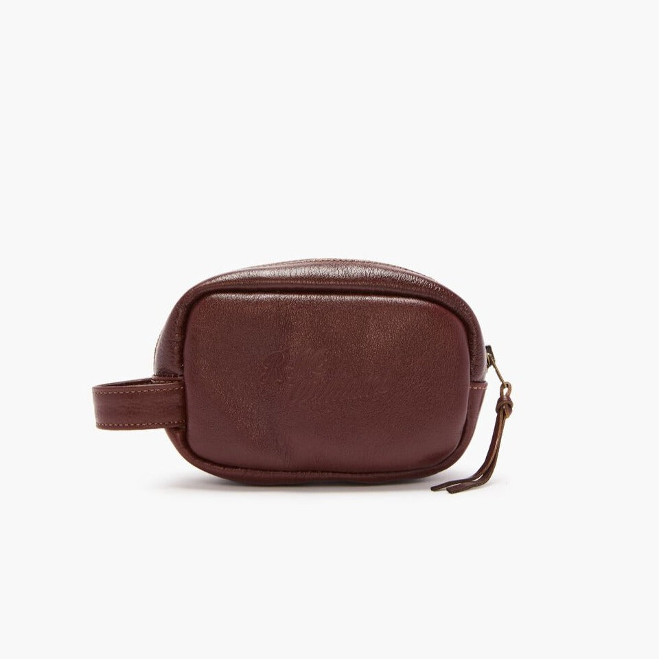 The RM Williams Mini Travel Care Kit includes a burgundy leather pouch with "R.M. Williams" embossed in the center, a tin of chestnut boot polish, a wooden brush with bristles, a smaller round brush, and a square leather cloth featuring a printed bull logo—perfect for caring for your R.M. Williams boots.