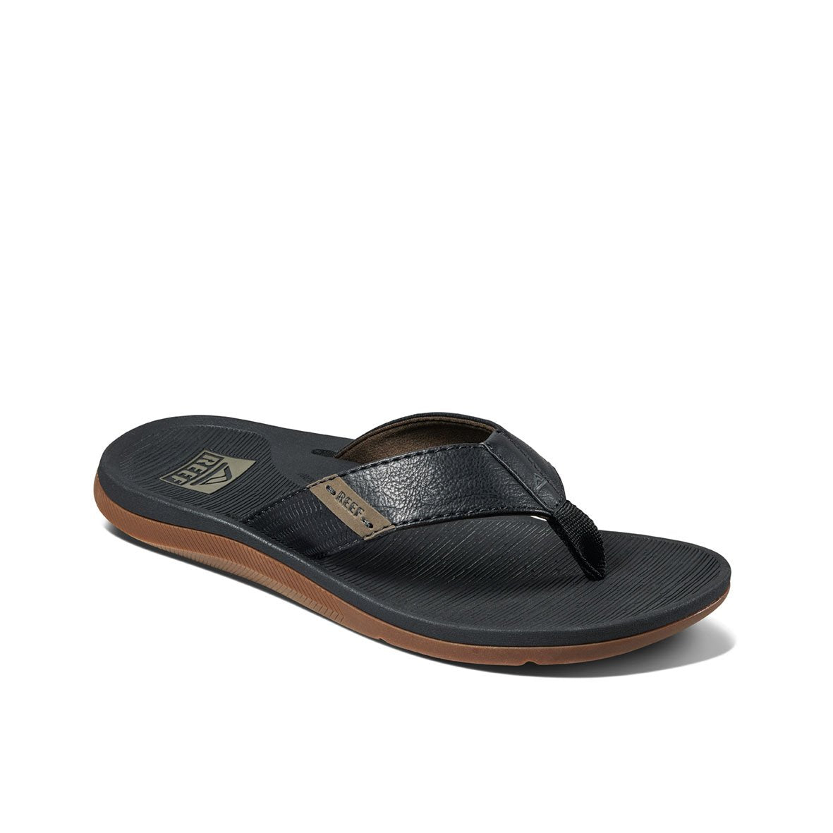 The REEF Santa Ana is a black flip-flop with brown and black sole detailing, featuring a strap made from black leather-like material. It includes a small logo tag on the side and has patterned grip on the footbed. These comfortable thongs offer arch support for added ease and present a sleek, modern design that is ideal for casual wear.