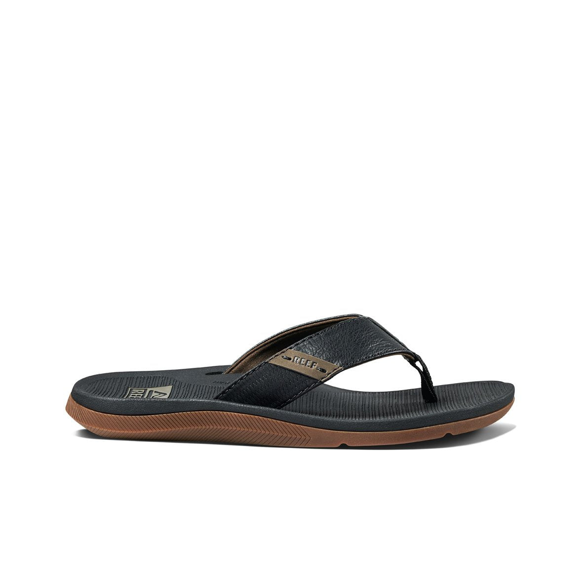 The REEF Santa Ana, a single black flip-flop sandal featuring a textured sole and brown trim, is displayed against a white background. The wide strap appears slightly padded for comfort, while the ribbed design of the water-friendly sole ensures traction. Additionally, these comfortable thongs offer excellent arch support.