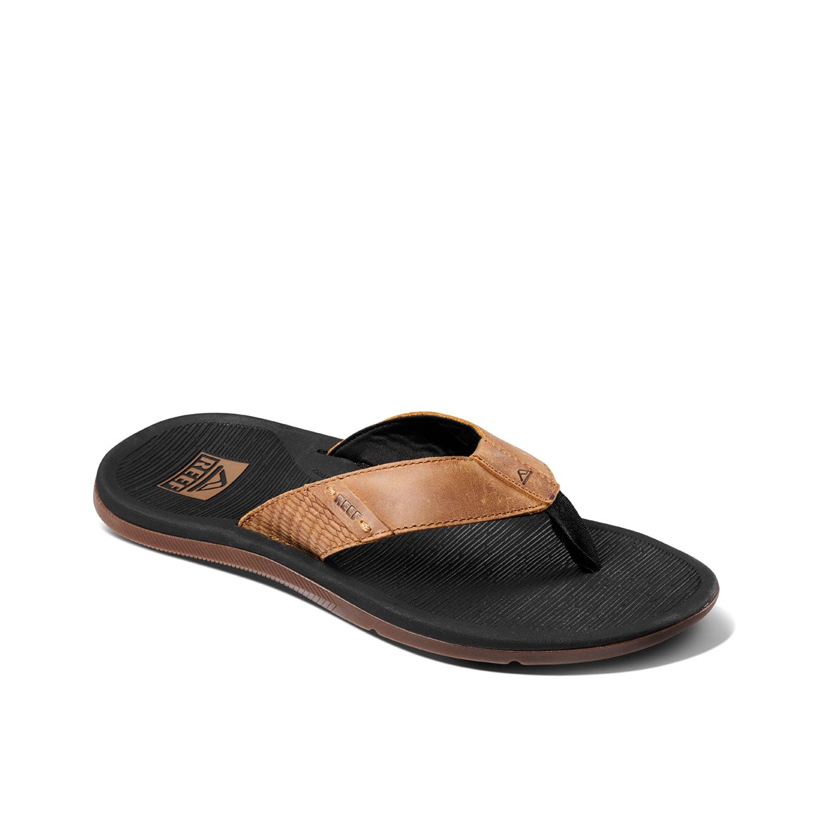 A single REEF Santa Ana LE flip-flop sandal is shown. The sandal features a brown leather upper strap with a small logo. Its sole is black with a grooved texture, and the footbed is slightly contoured for comfort and arch support. This water-friendly sandal offers a casual style, making it suitable for everyday wear.
