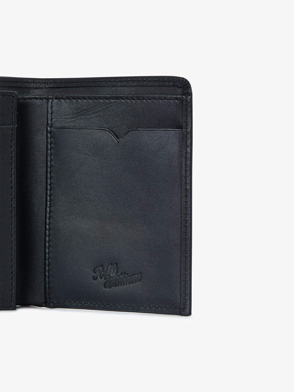 A close-up of the RM Williams Urban Small Slim Tri-Fold wallet in black full grain leather, highlighting the card slots and embossed logo on the bottom right corner.