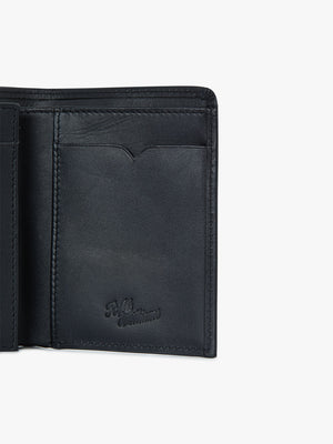 A close-up of the RM Williams Urban Small Slim Tri-Fold wallet in black full grain leather, highlighting the card slots and embossed logo on the bottom right corner.