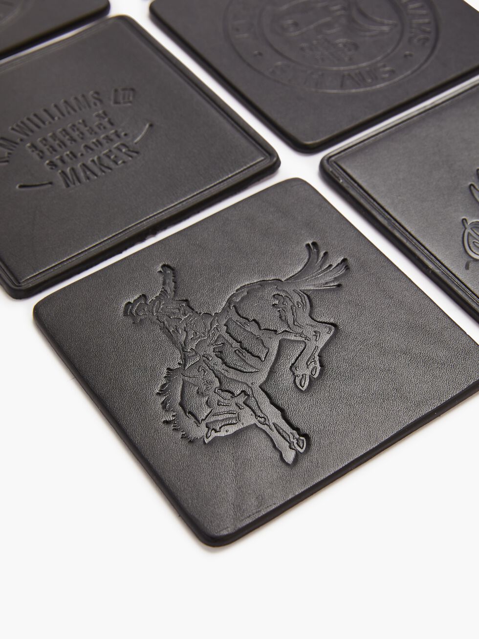 The RM Williams Heritage 6 Pack Coaster Set includes beautifully embossed black leather coasters. Some feature a cowboy on a bucking horse, while others display unique text and logos. Expertly crafted in Australia, these coasters stand out in an eye-catching grid pattern.