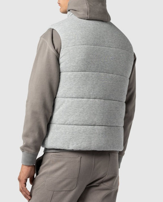 A person is seen from the back, wearing a gray hooded sweatshirt and gray pants, paired with the Rodd & Gunn Jackett Island Vest featuring high-loft synthetic insulation, against a plain light gray background. Their hood is down.