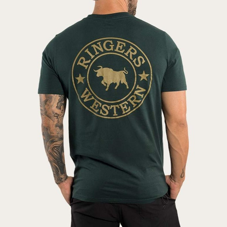 A man wears the Ringers Western Signature Bull Classic T-shirt, a dark green 100% cotton casual tee with a bull silhouette logo encircled by "Ringers Western" and stars on the back. The crew neck shirt pairs well with his tattooed arm and black pants as he stands facing away.