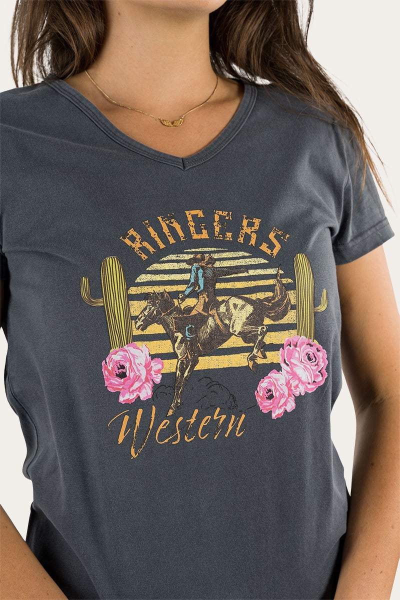 A woman wears the Ringers Western Rodeo Women's Relaxed V Neck Tee, a dark gray 100% cotton shirt with a cowboy on a bucking horse. It features bold "RINGERS Western" text, cacti, and pink roses for added charm.