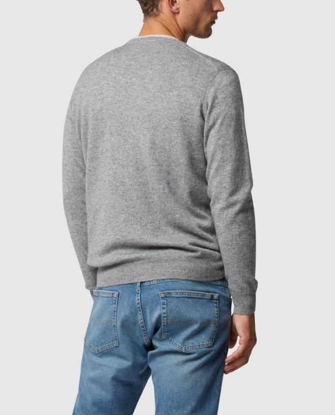 Dressed in the luxurious Rodd & Gunn Queenstown light gray cashmere sweater and blue jeans with distinct back pockets, someone is slightly turned away from the camera against a plain backdrop.