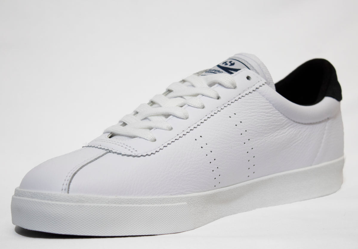 The Superga Clubs Comfleasueu Sneaker, in classic white leather with a black heel and crisp white laces, showcases subtle side perforations. Positioned at an angle against a plain white background, it exudes timeless style.