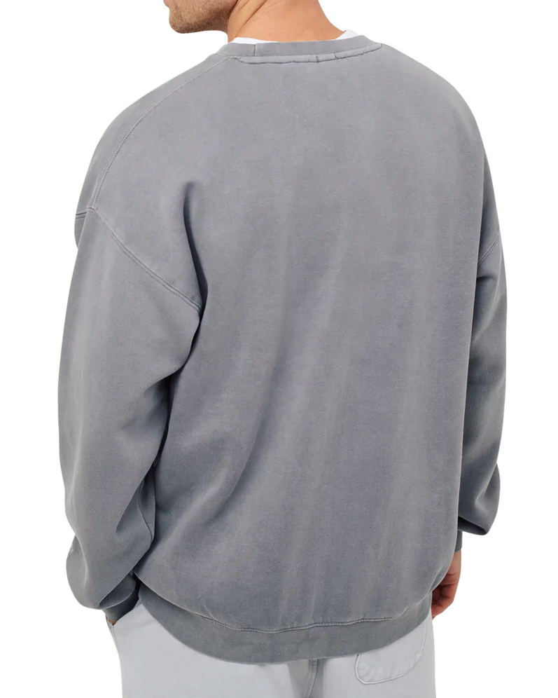 Someone in the Industrie The Del Sur Sweat, a baggy, relaxed fit acid wash gray sweatshirt with dropped shoulders and long sleeves, stands turned slightly away. It's paired perfectly with light-colored pants against a plain white background.