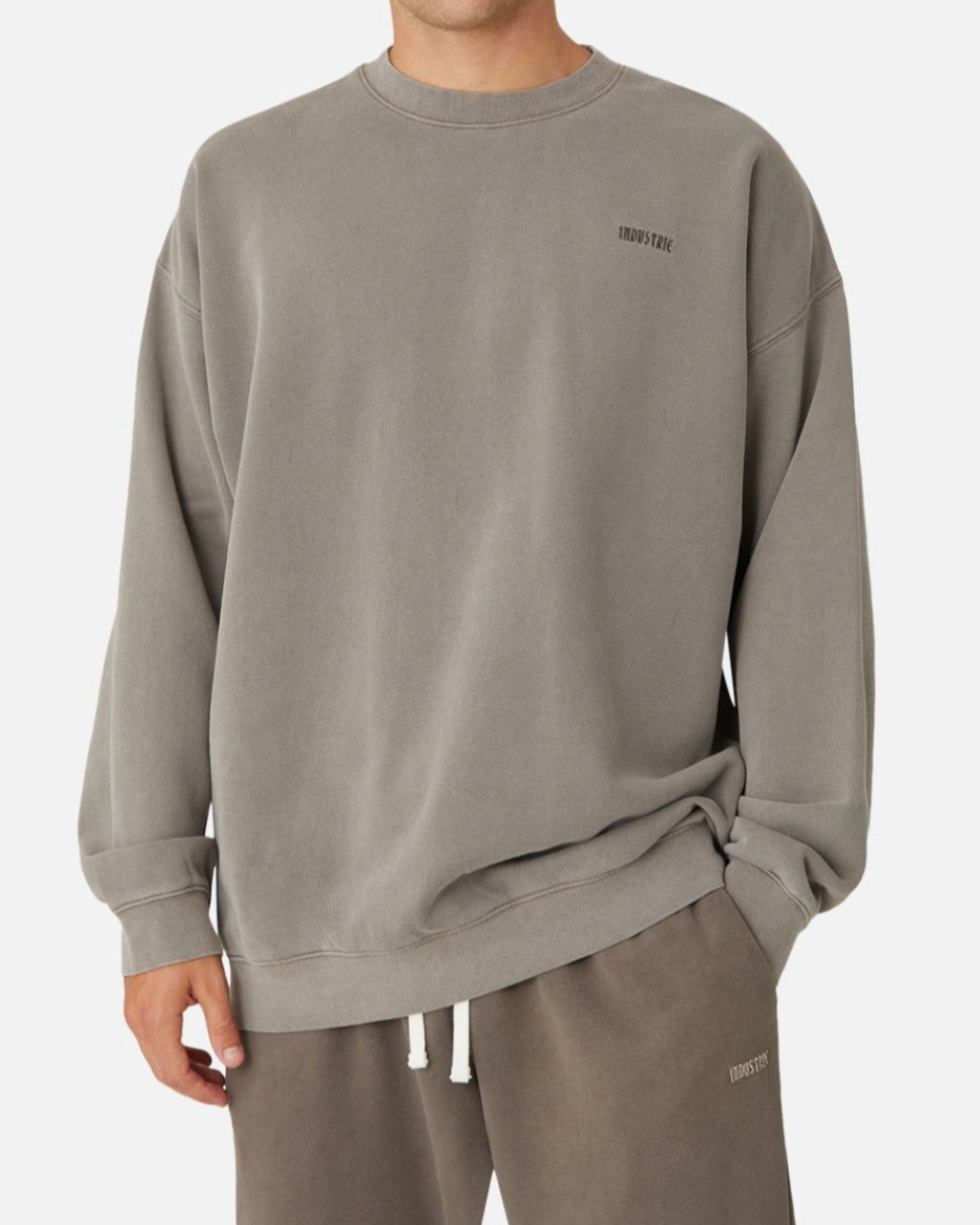 A person wears the Industrie The Del Sur Sweat, an oversized faded gray sweatshirt with soft fleece lining and subtle “INDUSTRY” text, paired with matching sweatpants, standing against a plain white background.