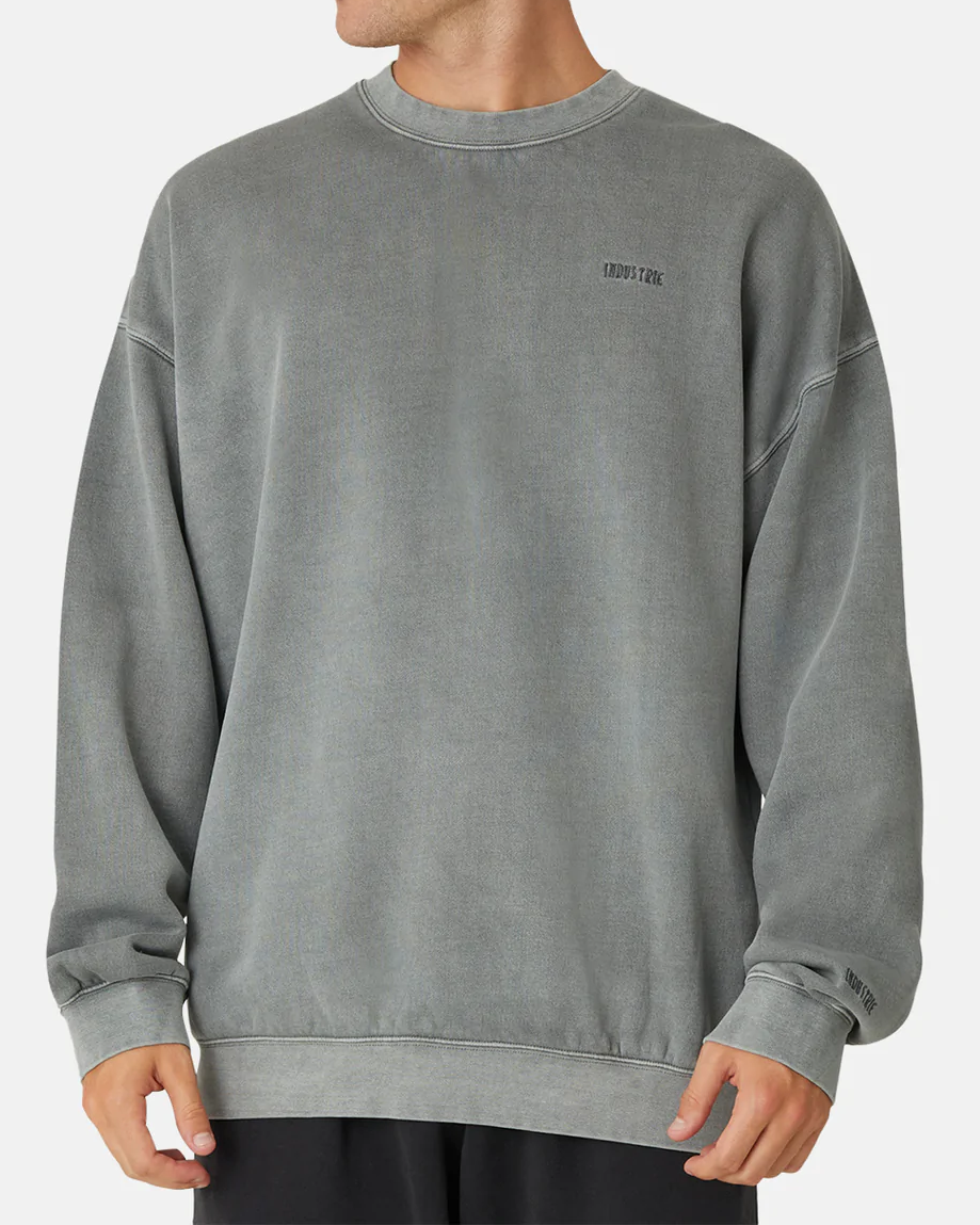 A person wears the Industrie The Del Sur Sweat in gray, with a comfy oversized fit and logos on the chest and sleeve, paired with black pants against a plain white background.