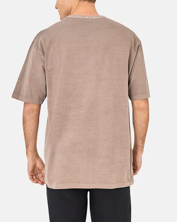 Someone is seen wearing the Industrie The Del Sur Tee, an oversized casual 100% cotton T-shirt in faded brown with a small neck label, paired with black pants, as they stand facing away against a plain white background.