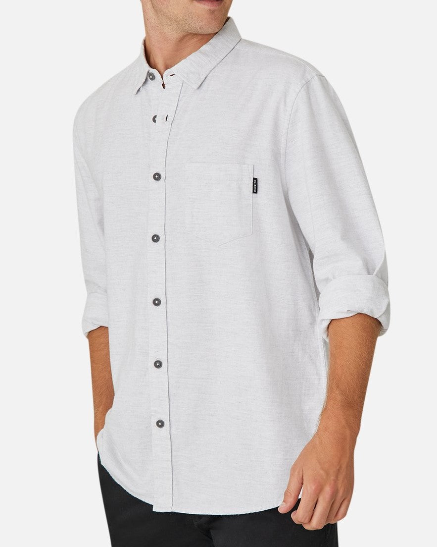 A person wearing the Industrie The Taylor Shirt, distinguished by its light gray long-sleeve button-up design and casually rolled-up sleeves. This 100% cotton shirt includes a front pocket adorned with a small tag and dark buttons, perfectly paired with dark pants for a comfortable and relaxed look.