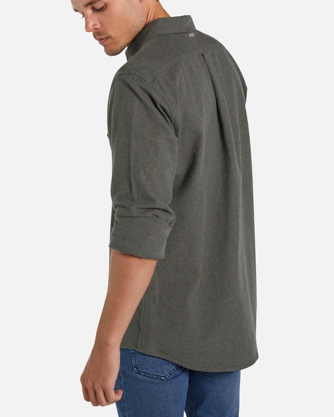 A man with short hair is wearing a long-sleeve, dark gray Industrie The Taylor Shirt and blue jeans. He is looking down over his right shoulder, with one arm slightly bent. The background is plain white.