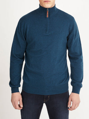 A person wears the RM Williams Ernest Sweater, a teal wool quarter-zip, with dark jeans, standing facing forward against a plain white background.