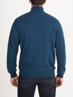 A person wearing the RM Williams Ernest Sweater—a blue wool, quarter-zip sweater—and dark jeans stands facing away from the camera against a plain white background.
