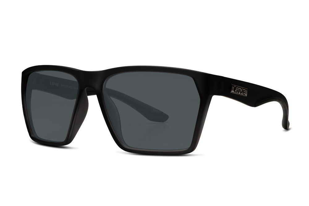 The Liive Rincon Sunglasses are black, rectangular with glossy dark lenses. They have thick arms adorned with a small metallic logo and are made from lightweight polycarbonate offering UV protection. Set against a plain white background, they are angled slightly to the side.