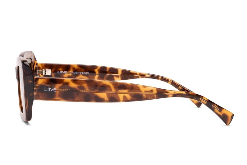 Side view of Liive Crush Sunglasses with tortoiseshell square frames and wide polycarbonate arms in brown and amber, emblazoned with "Liive CRUSH PM049" and "Liive" in white, providing stylish UV protection.