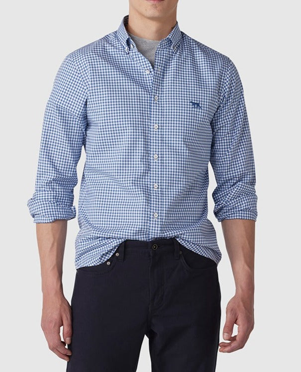 A person wearing the Rodd & Gunn Gunn Check Oxford Sports Fit Shirt, made of 100% cotton in a blue and white checkered pattern, with rolled-up sleeves and dark pants stands against a plain background. The stylish shirt features a small embroidered logo on the chest. The person's head is not visible in the image.