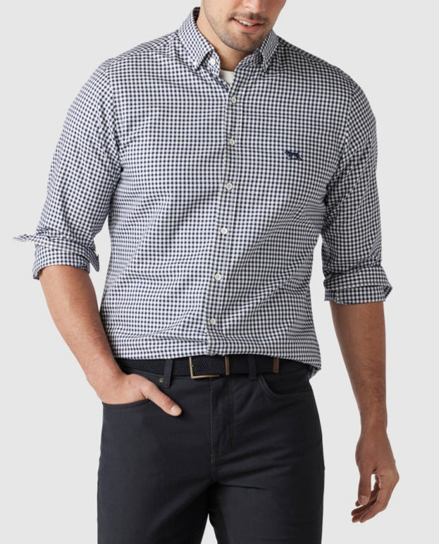 A man exudes confidence in a Rodd & Gunn Gunn Check Oxford Sports Fit shirt made of 100% cotton, standing against a plain background with rolled-up sleeves and dark pants that enhance his stylish look.