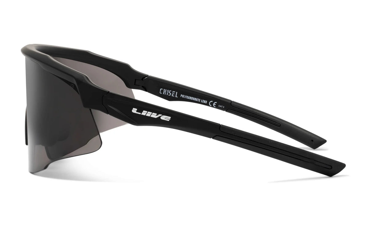 The Liive Z Chisel Safety Sunglasses have a sleek, wraparound black frame with "Liive" on the arm, featuring a single shatterproof dark lens providing UV protection. The angular design ensures a snug fit, perfect for outdoor activities.