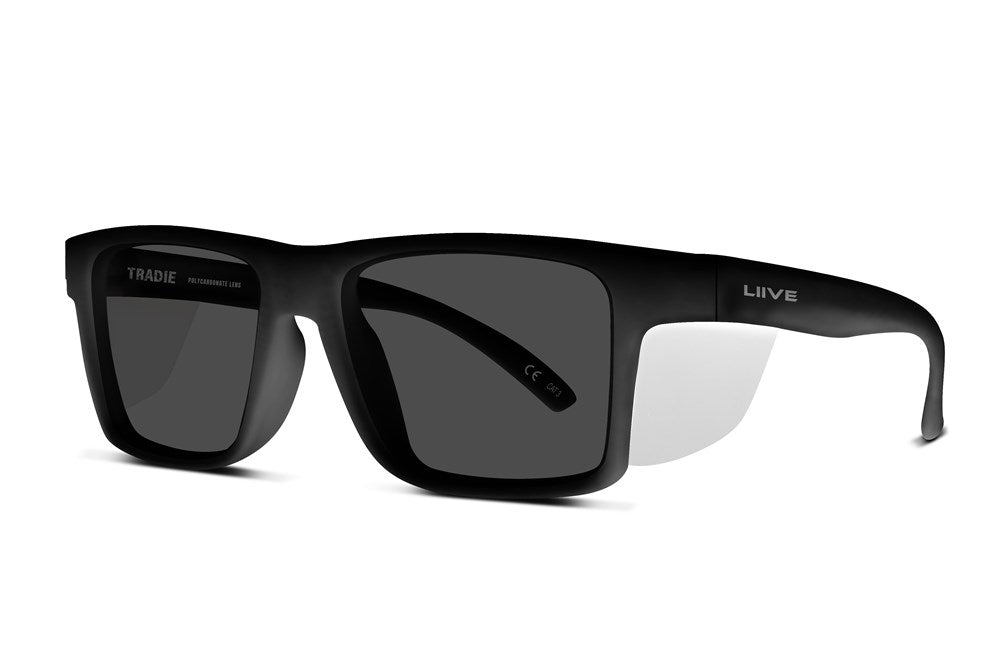 The Liive Z Tradie Safety Sunglasses feature a sleek black design with rectangular lenses, the brand names "TRADIE" and "LIIVE" on each arm, a durable polycarbonate frame, and shatterproof lenses offering tinted UV protection for style and safety.