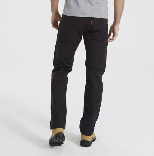 A person wearing a gray shirt, black pants, and beige shoes stands facing away from the camera. The photo highlights the back of their Levis Workwear 505 Utility Pant and beige shoes, designed for all-day comfort. The background is plain white.