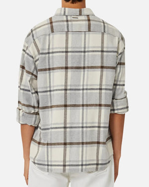 A person stands against a plain white background, wearing the Industrie The Elmhurst Shirt, a cream and gray plaid overshirt in brushed cotton. The sleeves are partially rolled up, enhancing its relaxed fit.
