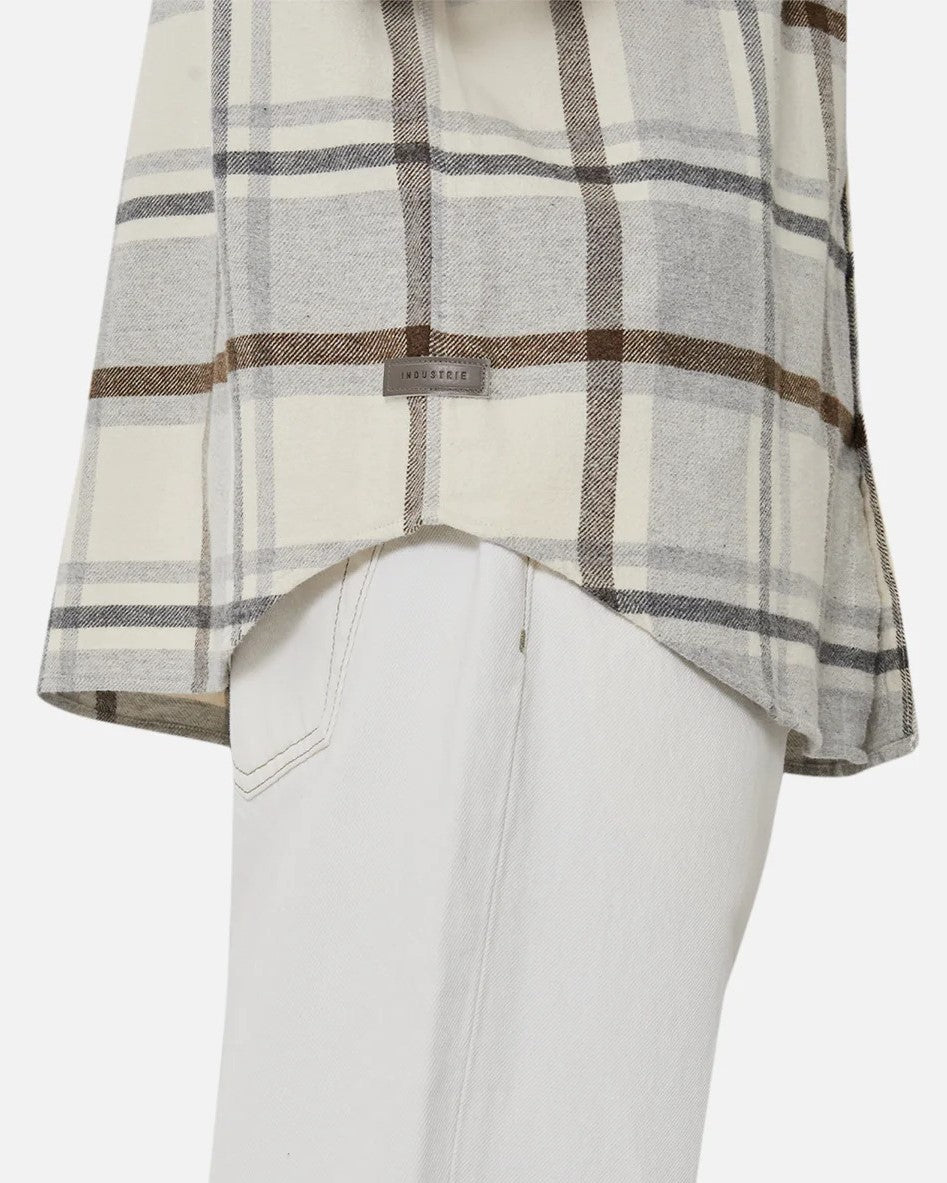 Close-up of a person in the Industrie The Elmhurst Shirt, a beige and brown plaid overshirt made from brushed cotton, paired with light pants. A small label is on the shirt's bottom. A plain white background emphasizes its relaxed fit and casual elegance.