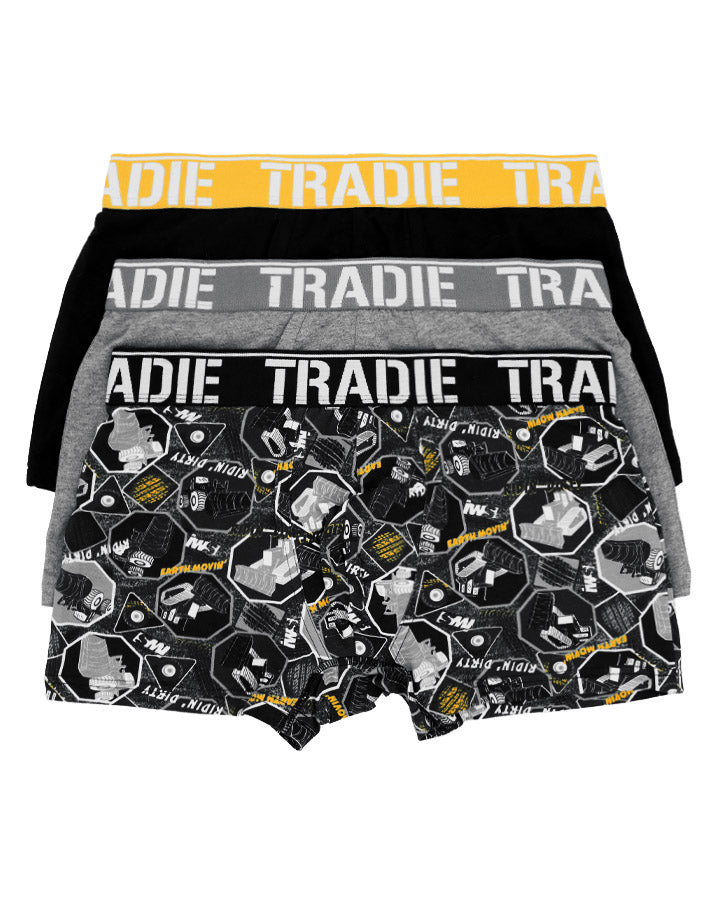 Four pairs of Tradie Men's Trunks are stacked. The top has a yellow waistband; the next two are gray and black with gray waistbands. The bottom pair features a bold black and white geometric pattern with tools and "NO DRAMA" text, crafted from a Cotton/Elastane blend.
