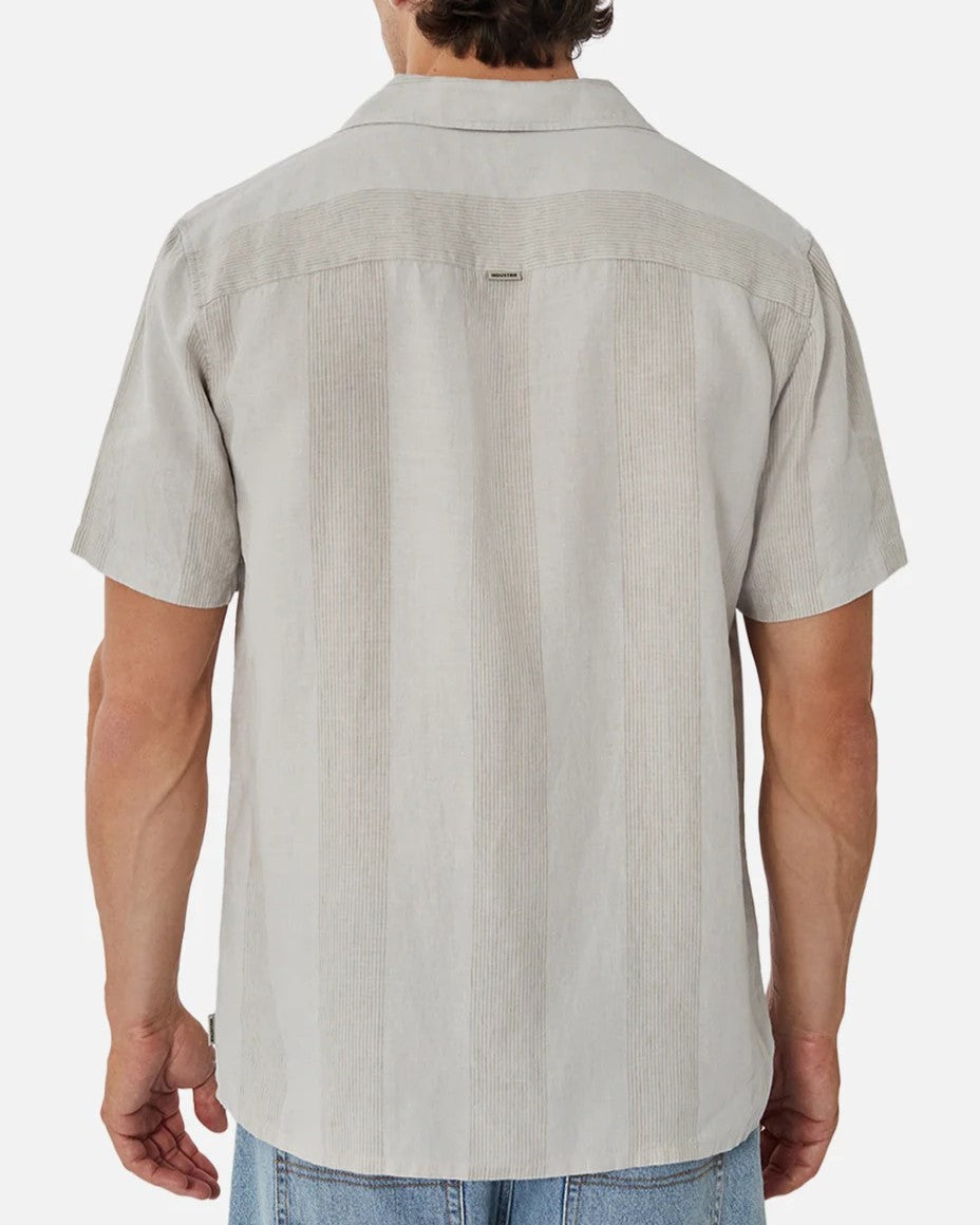 The image features a person wearing Industrie The Kanaki Short Sleeve Shirt in light gray with subtle vertical stripes, facing away to emphasize the back of the shirt, casually paired with blue jeans.