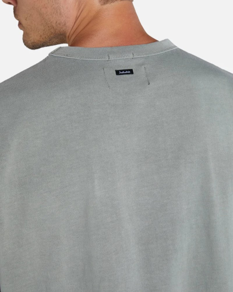 A person is shown from the back wearing an oversized light gray "Industrie The Del Sur Tee" featuring a small black tag with white text near the neck. The plain white backdrop highlights its relaxed, cozy vibe and laid-back appeal.