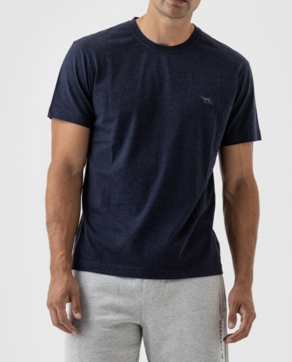 A person stands against a plain background in a Rodd & Gunn The Gunn T-Shirt, featuring a small logo on the chest. The dark blue, Australian Cotton casual tee complements their light gray sweatpants, with the individual visible from the waist up.