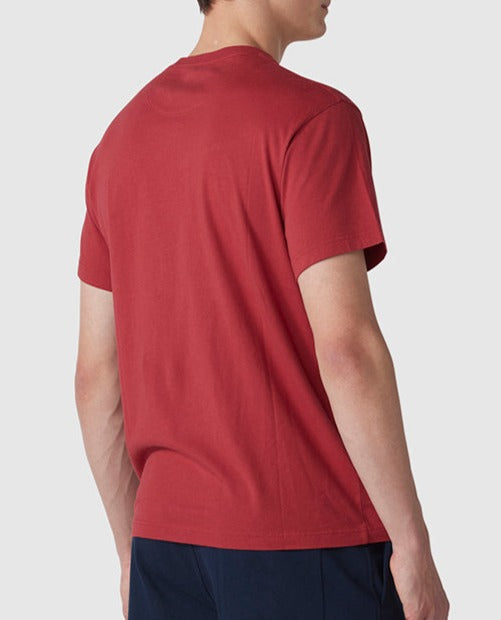 Man wearing a Rodd & Gunn Logo T-Shirt viewed from behind. He has short, dark hair and is also wearing dark blue pants. The background is plain gray.