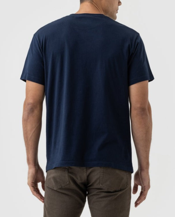 Facing away from the camera, an individual wears a navy Rodd & Gunn Logo T-Shirt of premium Australian cotton with brown pants against a white background.